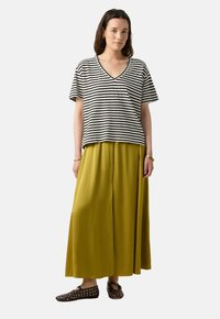 T-shirt à rayures noires et blanches avec un col en V, associé à une longue jupe jaune moutarde. Des chaussures marron avec des accents cloutés complètent la tenue.