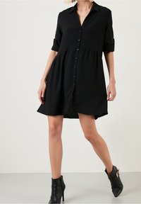 Vestito camicia nero con bottoni, dalla vestibilità comoda, maniche corte arrotolate e orlo svasato, realizzato in tessuto leggero e testurizzato.