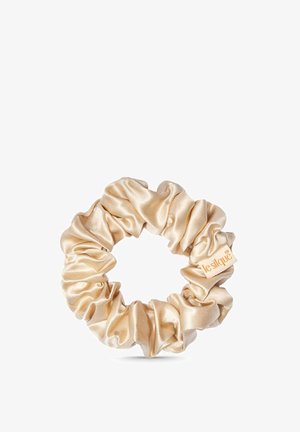 Beige satijnen scrunchie met een klein stoffen label met de tekst "leslique,", gerangschikt in samengevouwen cirkelvormige plooien op een witte achtergrond.
