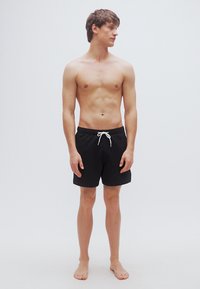 Μαύρο μαγιό σορτς με λευκό κορδόνι, απλός σχεδιασμός, μήκος μέχρι το μέσο μηρού, ελαφρύ ύφασμα, χωρίς ορατά σχέδια ή λογότυπα.