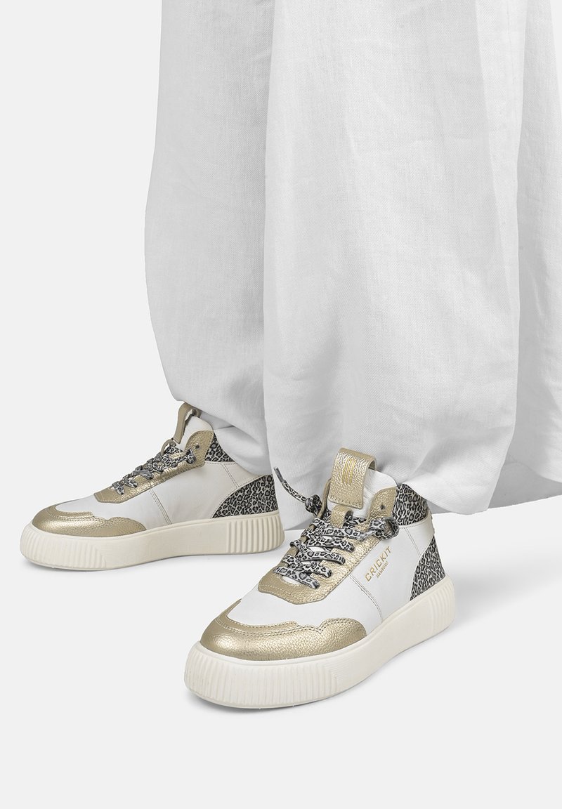 Białe sneakersy z metalicznymi złotymi akcentami, czarne detale w panterkę, szare teksturowane sznurowadła oraz masywna biała podeszwa.