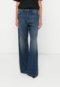 Blugi cu picior larg din denim albastru închis, cu o ușoară decolorare, design clasic cu cinci buzunare și închidere cu nasture metalic. Textură netedă.