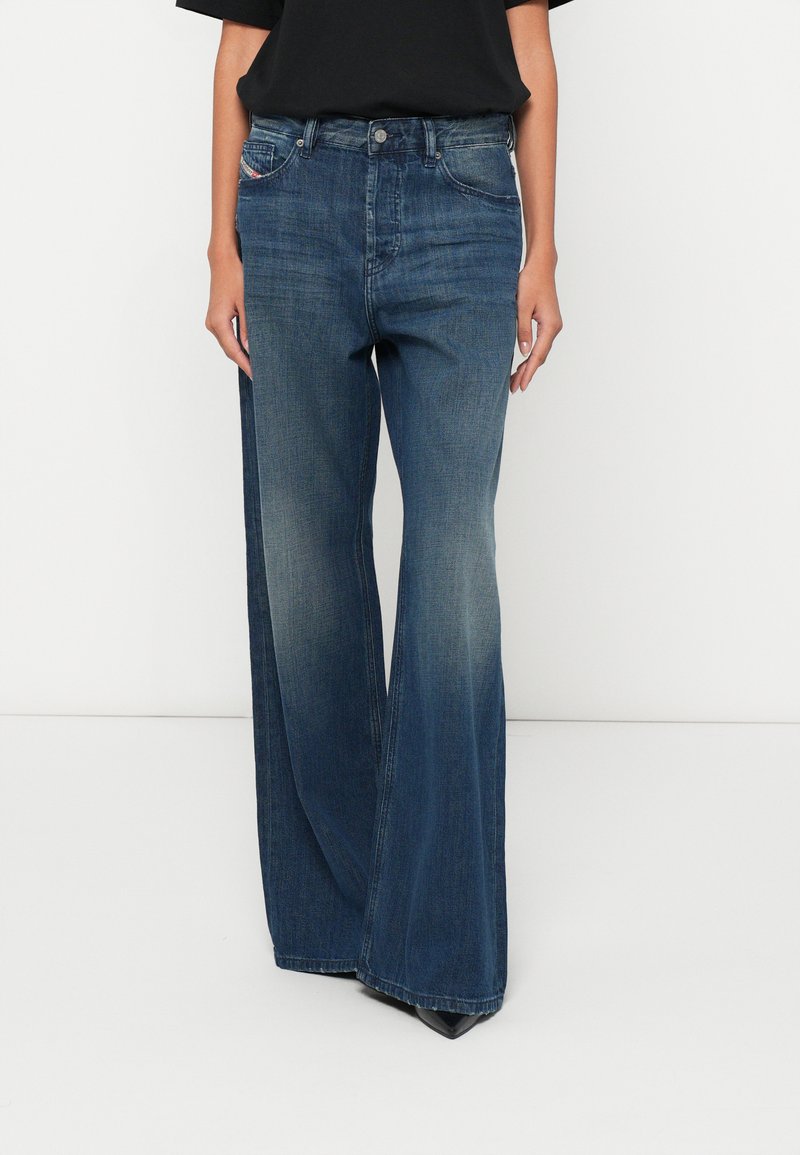 Blugi cu picior larg din denim albastru închis, cu o ușoară decolorare, design clasic cu cinci buzunare și închidere cu nasture metalic. Textură netedă.