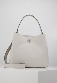 Sac fourre-tout structuré beige avec une texture lisse, une poignée supérieure unique et une bandoulière amovible. Présente un accent de logo circulaire.
