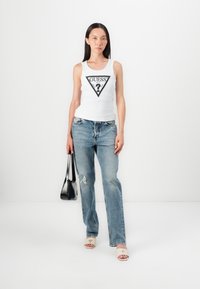 Top alb cu bretele, logo triunghiular negru, blugi decolorati bleu deschis, si mule cu toc bej. Geanta neagra cu bretele subtiri.