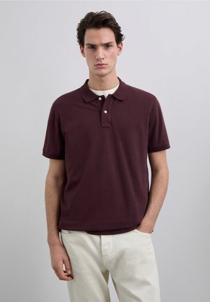 Polo bordeaux in cotone, con colletto classico, patta con due bottoni, maniche corte e un logo discreto sul petto.