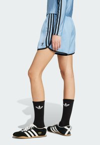 Ljusblå träningsshorts med svart kant, kombinerade med svarta strumpor med en vit logotyp, samt svarta och vita skor med tre ränder.