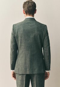 Tamsiai pilkas tekstūruotas kostiumas su pritaikytu siluetu, su išskirtiniu apykakle ir vienu ventiliacijos pjūviu. Švarkas derinamas su atitinkamais kelniais.