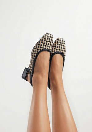 Pies con zapatos slingback de tacón bajo y bloque, con patrón tejido en negro y beige sobre un fondo claro.