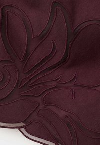 Tissu violet foncé avec broderie florale transparente présentant de grandes formes de pétales et de feuilles en gros plan.