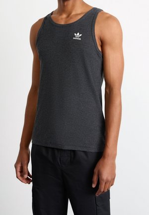Mann trägt dunkelgraues Adidas ärmelloses, geripptes Tanktop und schwarze Hose, von Hals bis Hüfte vor weißem Hintergrund gezeigt.