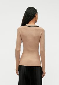 Κρεμ ριμπ πλεκτό πουλόβερ με μακριά μανίκια και λεπτομέρεια μαύρου γιακά, που ενισχύει τον εφαρμοστό σχεδιασμό και τη δομημένη σιλουέτα του.