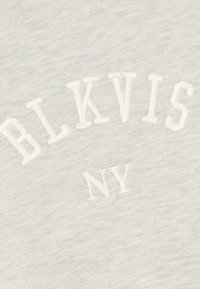 Világosszürke szövet puha textúrával, fehér hímzett „BLKVIS NY” szöveggel, ívelt elrendezésben.