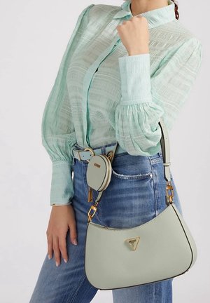 Sac à main vert clair de forme courbe, en matériau texturé, avec des détails en or et une pochette circulaire amovible, associé à un haut menthe et un jean.