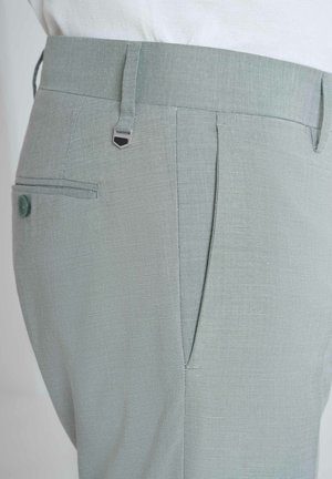 Pantaloni grigio chiaro realizzati in tessuto testurizzato, con una piega frontale, una tasca posteriore con bottone e un inserto metallico vicino alla vita.