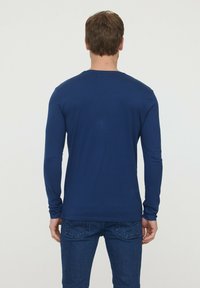 Chemise à manches longues marine en tissu doux, dotée d'un col rond et d'une coupe ajustée. Texture lisse avec peu de détails au dos.