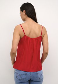 Rote Satin-Camisole mit dünnen verstellbaren Trägern und gerafftem Rückendetail, kombiniert mit blauen Denim-Jeans mit Rückentaschenstickerei.