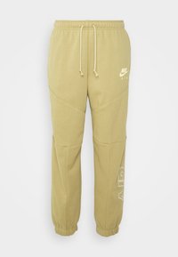 Nike Air sweatpants in light beige, featuring an elastic waistband with drawstring, tapered cuffs, and subtle logo accents on the front.