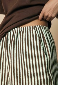 Hose aus leicht grünem und braunem gestreiftem Stoff mit elastischem Bund und Seitentaschen, die ein strukturiertes, zerknittertes Design zeigen.