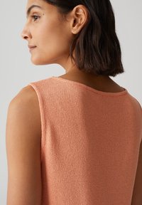 Top sans manches en tricot pêche avec un col rond, présentant un tissu texturé et de légères variations de ton sur toute la surface.