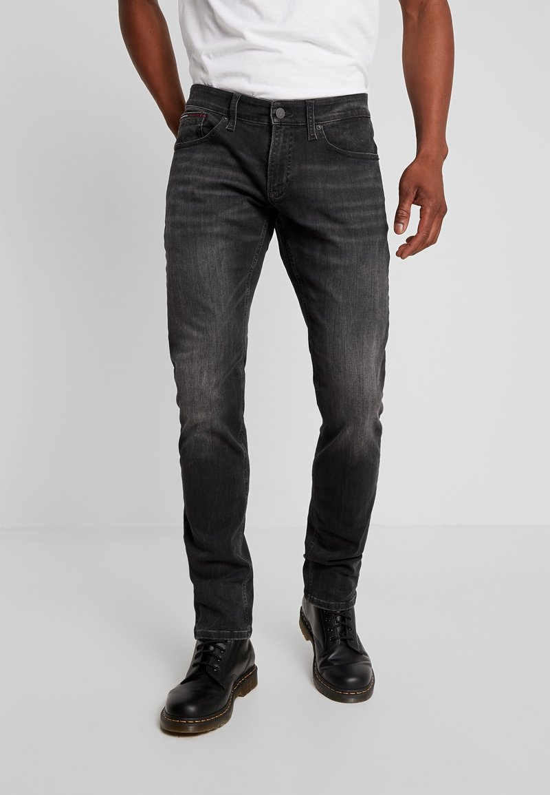 Mörkgrå denimjeans med slim fit, som har fem fickor, subtila slitningar och en knappstängning i midjan. Svarta läderstövlar fulländar looken.