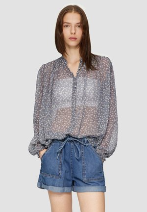 Blusa floreale trasparente in blu e bianco con scollatura volante e bottoni, abbinata a pantaloni corti in denim con vita elastica e tasche.