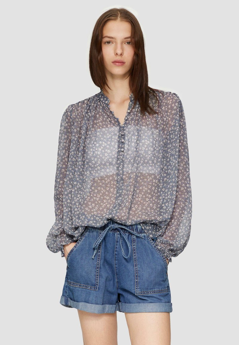 Blouse en dentelle florale bleue et blanche avec un décolleté volanté et des boutons, associée à un short en denim avec taille élastique et poches.