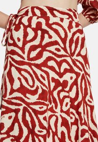 Falda con un patrón en rojo y crema que presenta un diseño en espiral, elaborada con una tela de textura suave y terminada con un detalle de cinturilla atada.