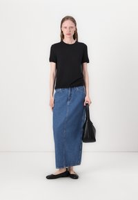 Svart t-shirt med kort ärm, ljusblå denim-maxikjol, svarta ballerinaskor och en svart väska, stående mot en helt vit bakgrund.