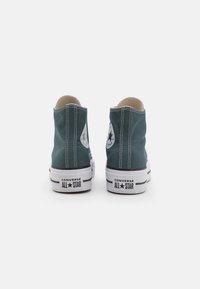 Zöld vászon magas szárú sportcipők fehér gumitalppal, fekete kiegészítőkkel és klasszikus logóval. A cipők oldalán kontrasztos varrás található.