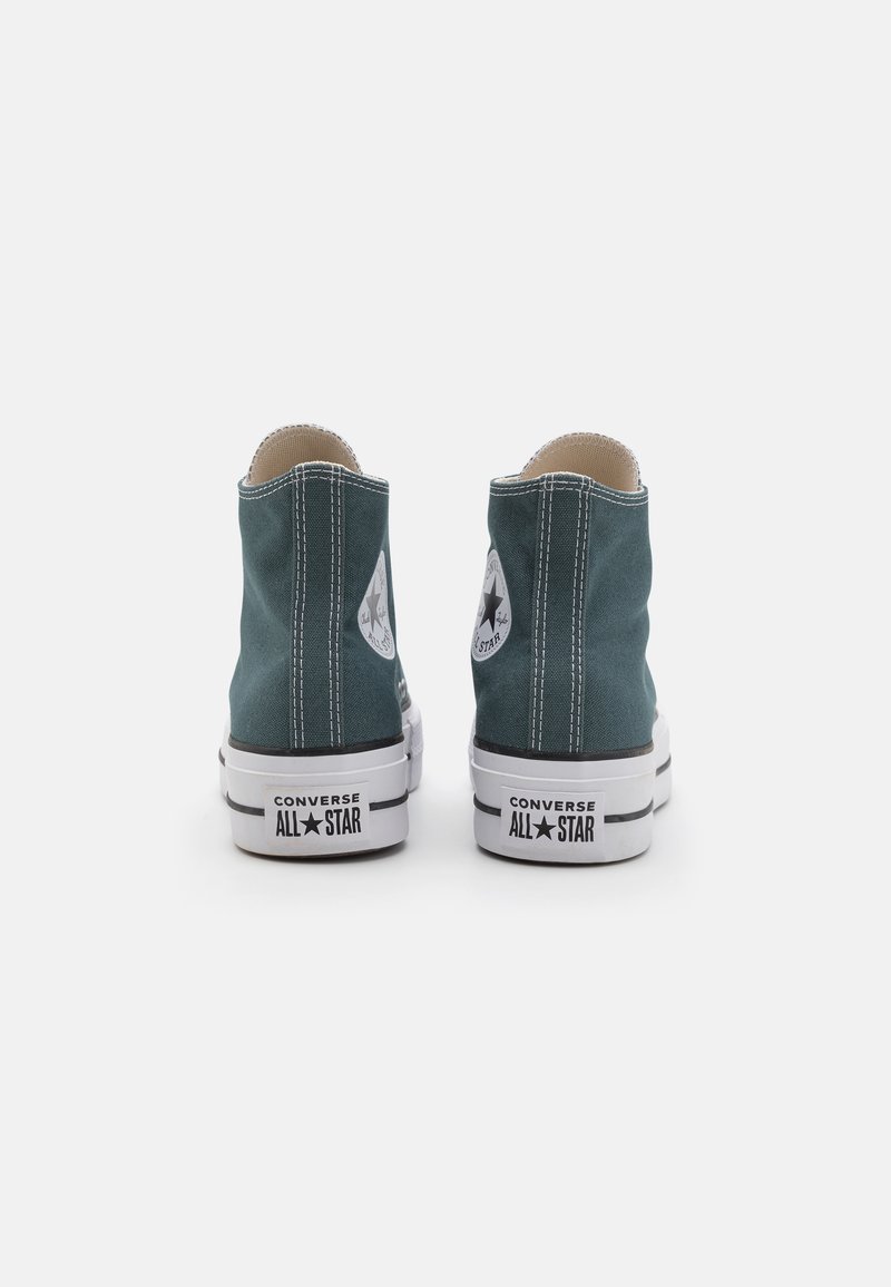 Baskets montantes en toile verte avec semelles en caoutchouc blanc, accents noirs et patch logo classique. Présente une couture contrastante sur les côtés.