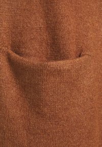 Tissu en tricot couleur rouille avec une texture douce, doté d'une poche proéminente. Le matériau présente un léger motif chiné pour un intérêt visuel.