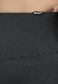 Leggings negras de talle alto con una textura suave y detalles de costura, que cuentan con una pequeña etiqueta negra con texto blanco en la cintura.