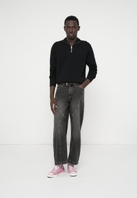 Maglione nero con collo a zip e jeans grigi aderenti con cuciture a contrasto; le scarpe da ginnastica rosa completano l'outfit. Design semplice e casual.