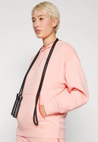 Rosa hettegenser laget av myk stoff, med kengurulomme og snorhette, med et svart hoppetau hvile mot den.