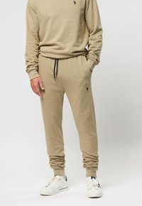 Beige katoenen sweatshirt en bijpassende joggers met elastische boorden en zwarte trekkoord. Klein logo-detail op de borst en dij.