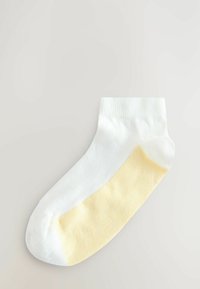 Witte enkelsok met een geel onderste gedeelte, met een gladde textuur en subtiele ribbels op de manchet. Minimalistisch ontwerp met contrasterende kleuren.