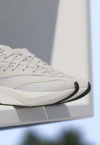 Gros plan de baskets blanches de sport avec des panneaux en mesh et cuir, semelle épaisse et lacets gris sur un rebord blanc avec un arrière-plan flou.