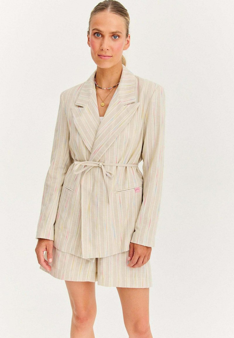 Pruhovaný blazer a odpovídající šortky v světlé béžové barvě s pastelovými akcenty. Měkká tkanina, přední kapsy a detaily se zavázáním v pase.