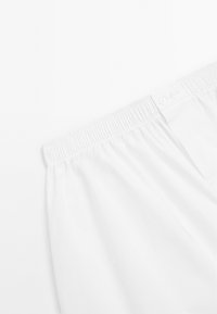 Bílé kalhoty s elastickým pasem, které mají zapínání na knoflík a hladkou texturu, zdůrazňující klasický, minimalistický design.
