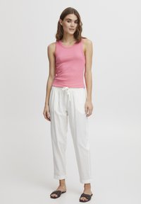 Débardeur rose associé à un pantalon blanc ample avec un cordon de serrage. Des sandales noires à glissière complètent la tenue. Design simple et décontracté.