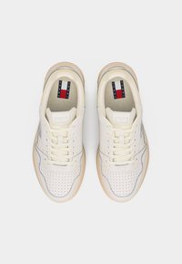 Paire de baskets Tommy Jeans blanc cassé avec boîte à orteils perforée, semelles beiges et lacets, vues de dessus sur un fond blanc.