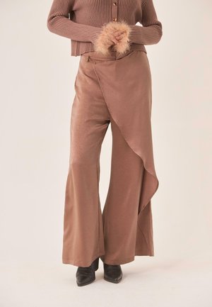 Pantalones marrones de pierna ancha con un detalle envolvente asimétrico, combinados con un suéter acanalado y botines negros de punta puntiaguda.