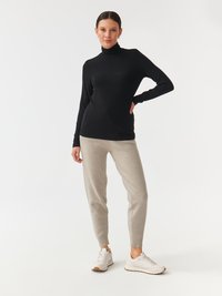 Črni pulover s turtleneck ovratnikom, v kombinaciji s svetlosivimi jogger hlačami, ki imajo oprijet kroj in elastične manšete, dopolnjene z belimi športnimi čevlji.