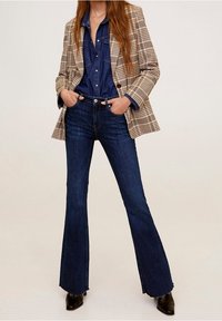 Vaqueros oscuros acampanados combinados con un blazer de cuadros beige y una camisa de mezclilla abotonada, mostrando un ajuste a medida y texturas contrastantes.