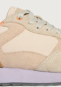 Sneaker beige e grigio chiaro con pannelli in suede e tessuto, lacci grigi e suola lilla su uno sfondo semplice.
