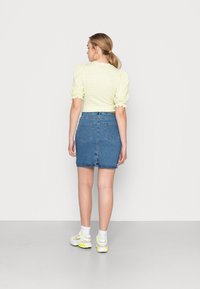 Camisola curta de manga curta em xadrez amarelo com mangas bufantes, combinada com uma saia mini em denim azul. Ténis brancos com toques de néon completam o visual.