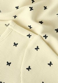 Geribbelde crèmekleurige trui met zwarte vlinder motieven. Zachte textuur met een klassieke ronde hals en subtiele stikdetails.