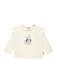 Long-sleeve cream shirt with ruffled shoulder accents and a bear graphic printed in dark colors. Features snap closure at the neck.
