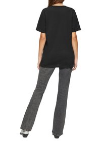 Zwarte katoenen t-shirt met een relaxte pasvorm, korte mouwen en een ronde halslijn, gecombineerd met donkergrijze uitlopende jeans en zwarte schoenen.